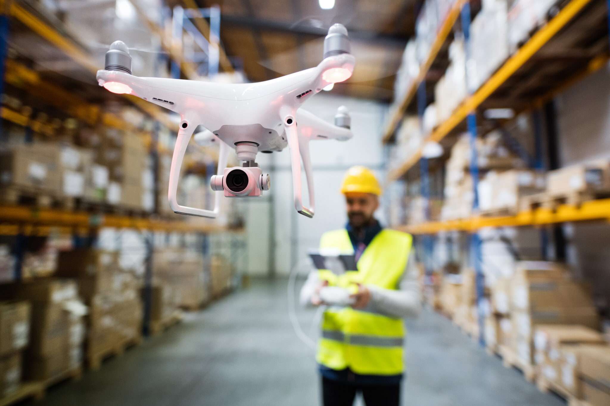 The warehouse worker is using the autonomous drone for inventory management task.