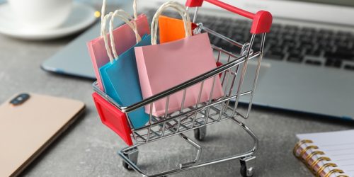 Composition with small shopping cart and paper bags on grey background, space for text